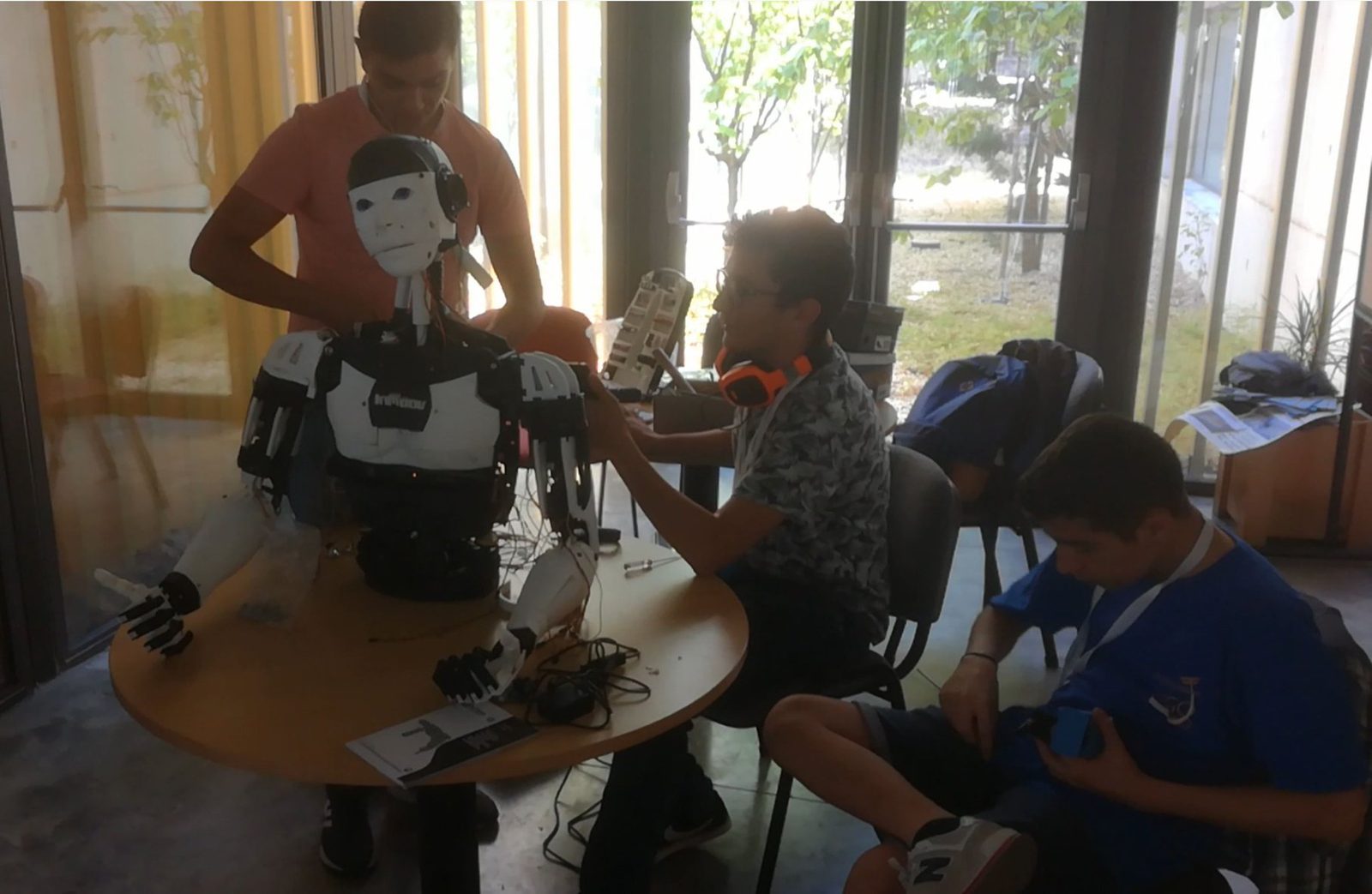 Three club members working on the robot's torso and arms around a round table before a demonstration.