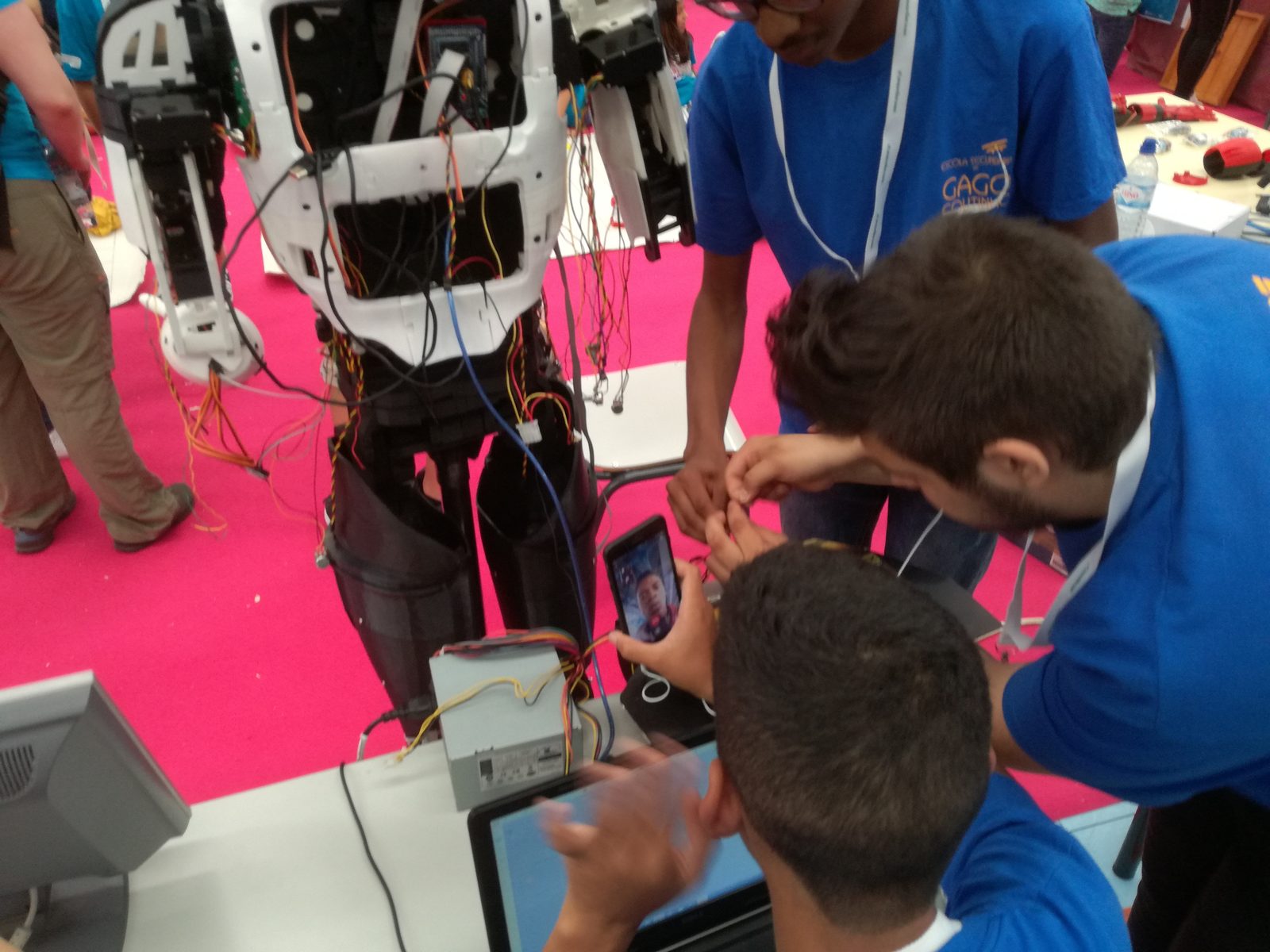 Team members crouched around the robot's exposed torso wiring, debugging during the event.