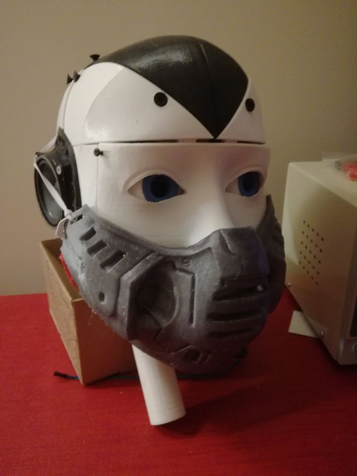 A printed white robot head with blue eyes and a black hairpiece, wearing a grey armoured face mask.